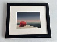 Framed painting of a red canoe on a shore against a gradient sky, shown in a black frame with white matting.