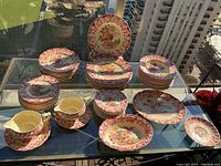 Overhead view of full dinnerware set on glass table, showing stacks of plates, bowls, platters and accessories