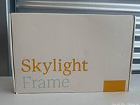 White box with yellow 'Skylight Frame' branding on front for the picture frame.