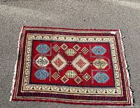 Top view of the small Navajo-style southwestern area rug showing the red, cream, blue, yellow, and green geometric pattern with visible wear and frayed edges.