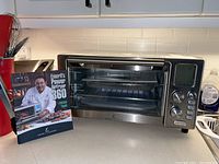Emeril Lagasse Power AirFryer 360 with the recipe book shown on the left side on a kitchen counter.