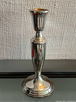 Front view of a tall polished sterling silver candlestick holder showing the shape and bright reflective surface.