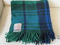 Folded wool blanket in Black Watch tartan with fringe edges, showing overall pattern and color scheme.