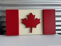Front view of wooden Canadian flag wall decor showing red painted maple leaf centered on white backboard with red side panels.