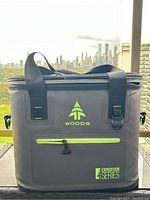 Front view of Woods Expedition Series soft shell cooler showing green logo, zipper pocket, and carrying straps.