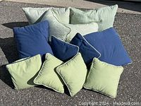 All 12 blue and green throw pillows displayed outdoors, showing varied sizes and patterns including solid blue, solid light green, striped, and checkered fabric.