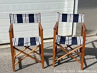 Pair of vintage director's chairs with wooden frames and blue and grey striped fabric seat and backrest photographed outside on pavement in front of a garage door.