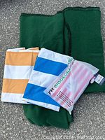 Overview of all items showing two green fleece blankets folded and three striped quick dry towels, including biodegradable packaging bag.