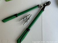 Pair of garden shears in green and black with two metal boat cleats placed on a white surface.