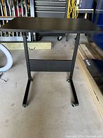 Front view of a black adjustable small table on locking wheels, showing rectangular top and metal frame.