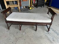 Front view of antique mahogany bench with cushion showing turned legs and arms