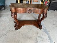 Front view of antique buffet table showing detailed carvings, curved edges, and claw feet.