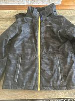 Dark gray boys snow suit jacket with yellow zipper and two front zippered pockets shown on a table.