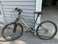 Side view of gray KHS kids mountain bike with front shocks, tires, saddle, and pedals visible.