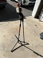 Photo showing the microphone mounted on the adjustable tripod stand on a concrete floor in daylight.