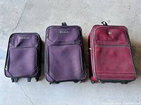 Photo of three soft-sided suitcases placed on floor showing front view of two purple Samsonite bags and one maroon suitcase.