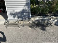 Three metal shoe/boot racks shown side by side outdoors on pavement in front of a gray building. Racks consist of metal tubing and mesh wire shelving, each has three tiers.