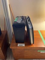 Side view of black paper shredder and silver Samsonite briefcase on wooden table.