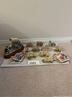 Photo showing entire collection of miniature houses, cottages, sheep herding dog figurine, square coasters and book arranged on grey mat.