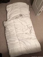 Full view of the white quilted duvet comforter lying open on a carpeted floor, showing stitching and fabric texture.