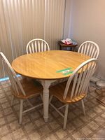 View of the round wooden farmhouse dining table with four matching chairs, showing white painted legs and natural wood top.