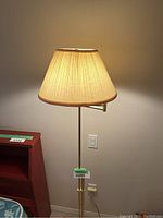 Side angle view focusing on the lit beige fabric shade and gold lamp post, highlighting texture and color.