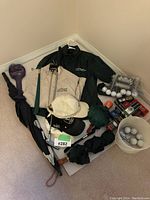Full lot showing golf jackets, golf balls, putter, umbrellas and caps on carpet floor corner.