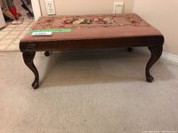 Front view of the wooden needlepoint bench showing carved legs and floral needlepoint upholstery.