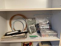 Shelf showing various needlepoint craft supplies including embroidery hoops, canvas, kits, thread organizer, and needles.