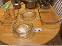 Overhead view of four glass baking pieces on wooden table, including measuring cup, pie plate, round bowl and rectangular dish