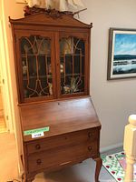 Front view of the antique wooden secretary desk showing glass hutch, decorative wood panels on glass doors, and two lower drawers.