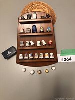 Full view of wooden rack mounted on woven panel holding 3 rows of 18 thimbles and 5 placed on table