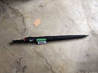 Full length view of the closed black and red golf umbrella on concrete floor with handle visible.