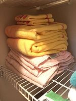 Stack of yellow and pink bath towels on closet shelf.