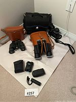 Full lot view showing black Minolta camera, three sets of binoculars, leather and fabric cases, and black carrying bag