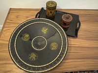 Overview of 4 Burmese lacquerware pieces on wood table including large bowl, 2 containers on tray, and rectangular tray.