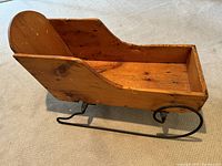 Side view of antique pine wooden sled with wrought iron runners, showing smooth curved sides and solid backrest.