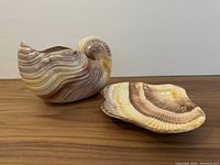 Front angled view of shell shaped ceramic vase and matching dish on wooden surface.