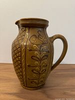 Front view of large vintage ceramic water jug showing floral and geometric tube lining decoration, handle, and spout.