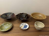 Lot of six vintage studio pottery pieces displayed on wood surface, including various shapes and glazed finishes for detail inspection.