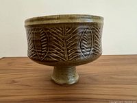 Side view of mid century footed pedestal bowl showing carved leaf and fern designs on brown glaze
