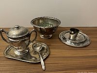Photo showing large sugar bowl with lid and handles on matching tray with jelly spoon alongside round flower bowl with inserted flower frog and baby christening cup on warming dish.