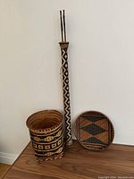 Full lot displayed: square rivercane basket, round basketry tray, quiver with two arrows leaning against a wall on wood surface