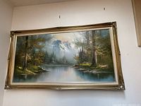 Full view of the large landscape oil painting in its gold ornate frame hanging on a white wall.