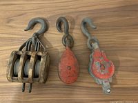 Three vintage industrial metal pulleys arranged on wooden surface, showing hooks and wheels