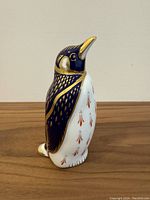 Side view of Royal Crown Derby bone china penguin figurine showing cobalt blue and gold detailed painting and white body with red patterned accents.