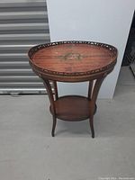 Full view of antique wooden side table showing the oval top with floral painting and pierced metal rim with visible missing section.