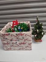 Fabric Christmas-themed box filled with various holiday decorations and a mini artificial Christmas tree decorated with small stars and snowflakes.