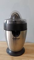 Front view of stainless steel Cuisinart electric citrus juicer with clear plastic lid on wooden surface.