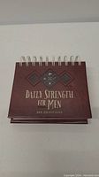 Front cover of the daily devotional flip calendar titled 'Daily Strength for Men 365 Devotions' in brown with embossed design and text.